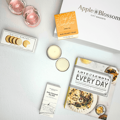 No place like home gift box includes sparkling tea, sunshine tea, lemon shortbread cookies, candle sea salt and every day cook book in a signature Apple Blossom gift baskets luxury gift box.