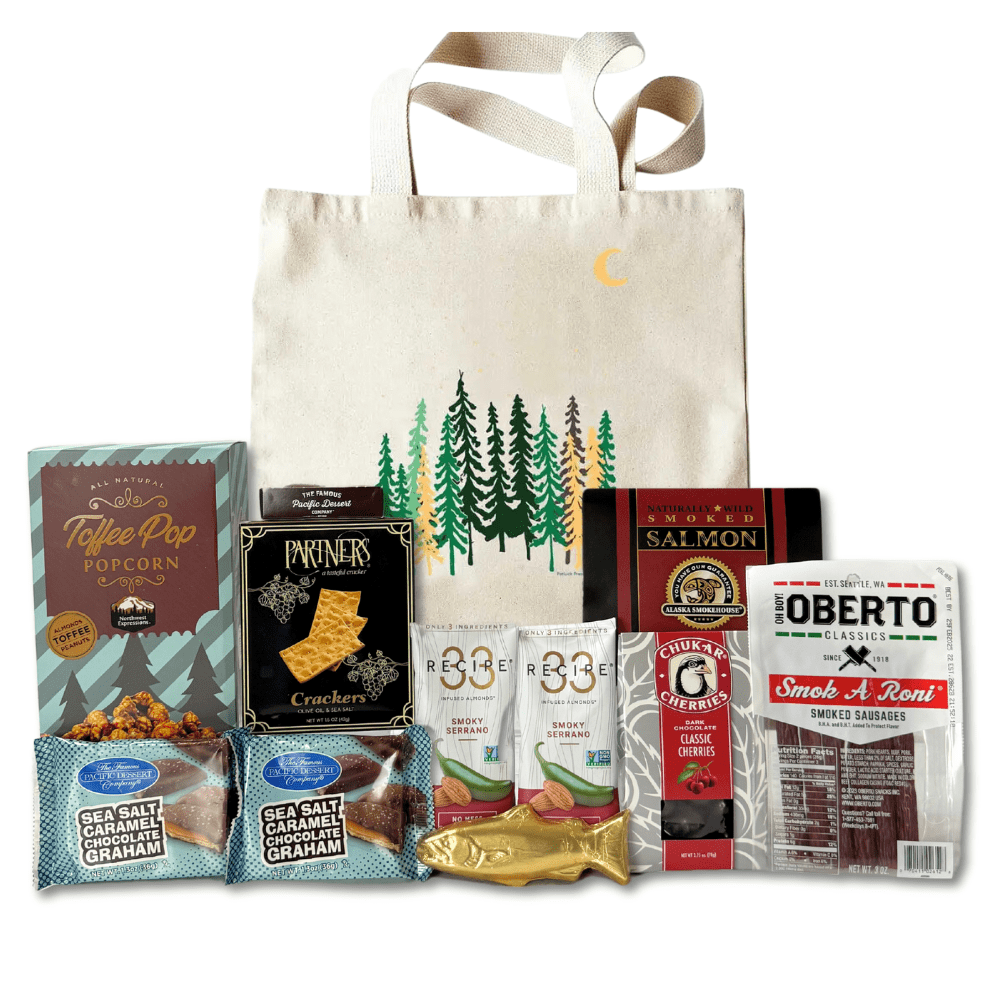 made in washington gift tall trees pnw canvas tote with local snacks caramel corn, pepperoni sticks, smoked salmon, solid chocolate salmon, smoked almonds, chocolates, crackers and more.