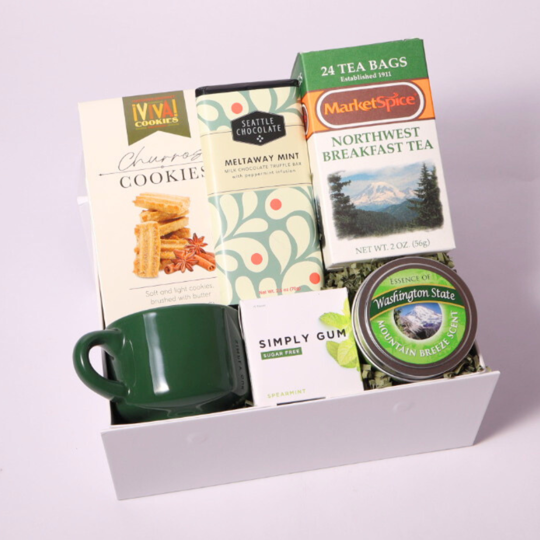 Gift box featuring locally crafted Pacific Northwest treats, including MarketSpice tea, Seattle Chocolate mint bar, soy candle, churro cookies, and a ceramic teacup. Perfect for tea lovers and relaxing break times.