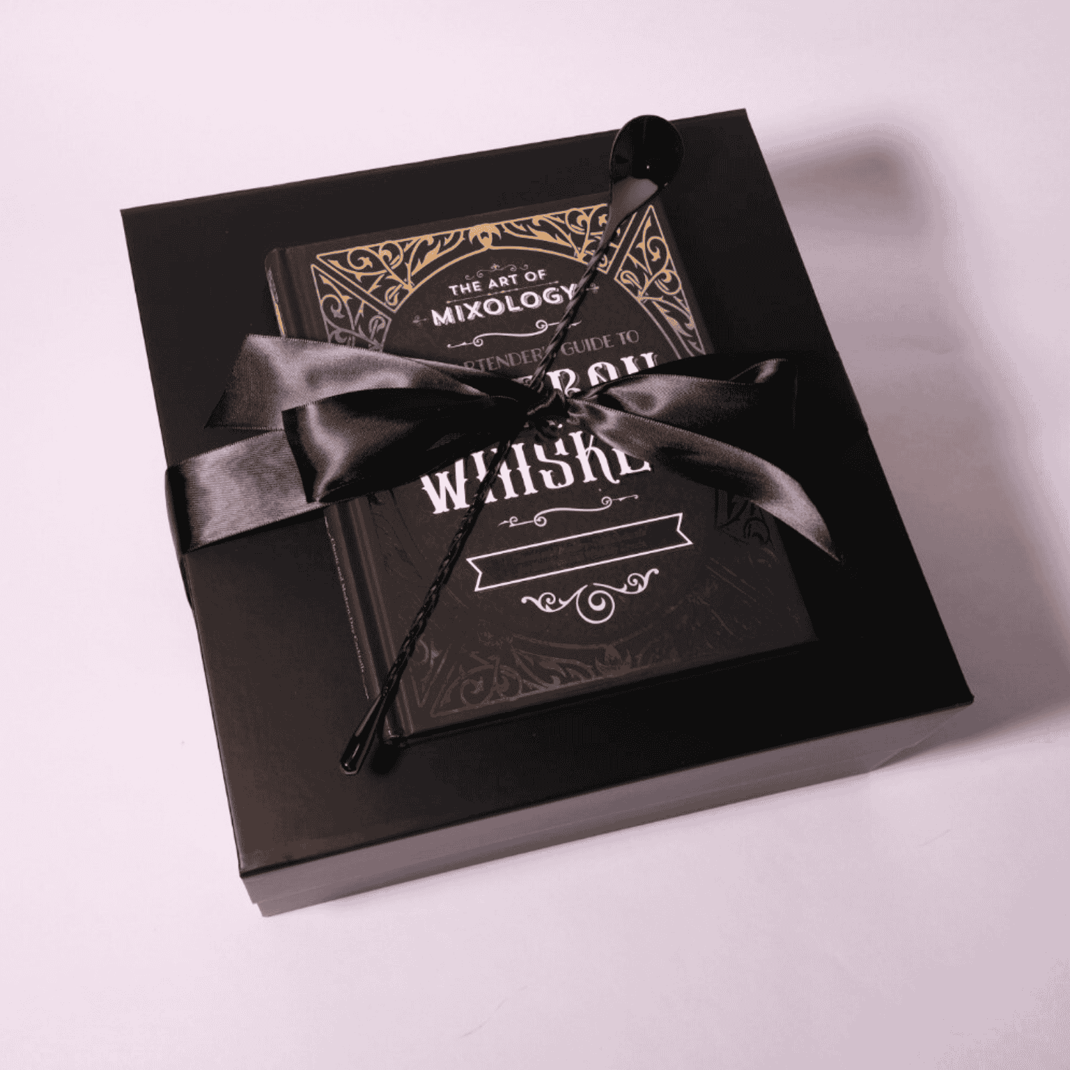 Luxury whiskey gift box wrapped with a black satin bow, featuring the cocktail recipe book and bar spoon elegantly displayed on top, perfect for gifting.